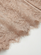 Detail shot of beige lace lingerie featuring a delicate eyelash lace hem and smooth satin piping. Sheer nude floral fabric highlighting elegant craftsmanship in women's intimates, bodysuits, and corset designs.