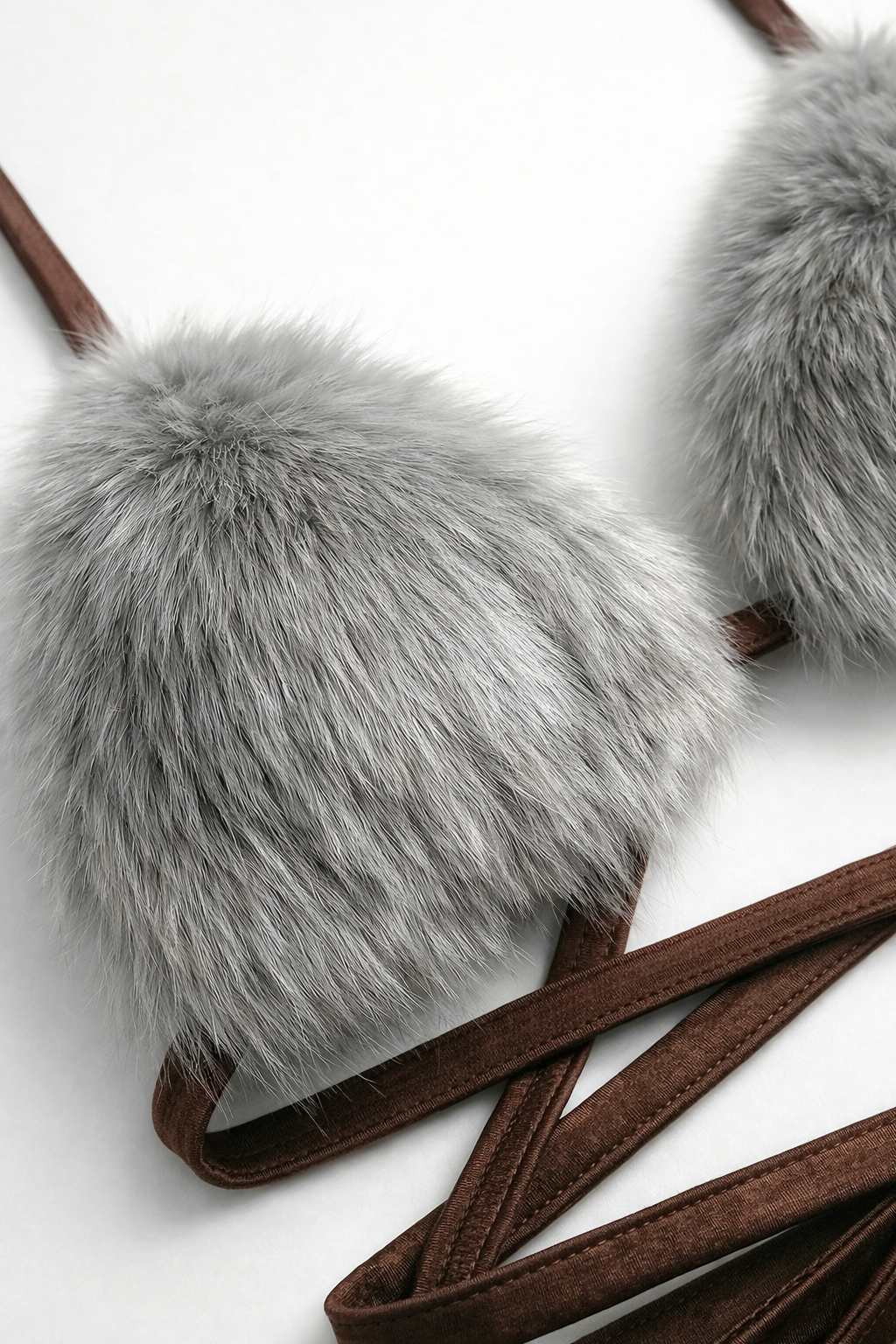 Close-up shot of a unique bralette top featuring fluffy grey faux fur cups and long, strappy brown wrap ties. Detail of exotic women's lingerie, festival wear bikini construction, and playful intimate apparel designs.