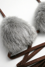Close-up shot of a unique bralette top featuring fluffy grey faux fur cups and long, strappy brown wrap ties. Detail of exotic women's lingerie, festival wear bikini construction, and playful intimate apparel designs.