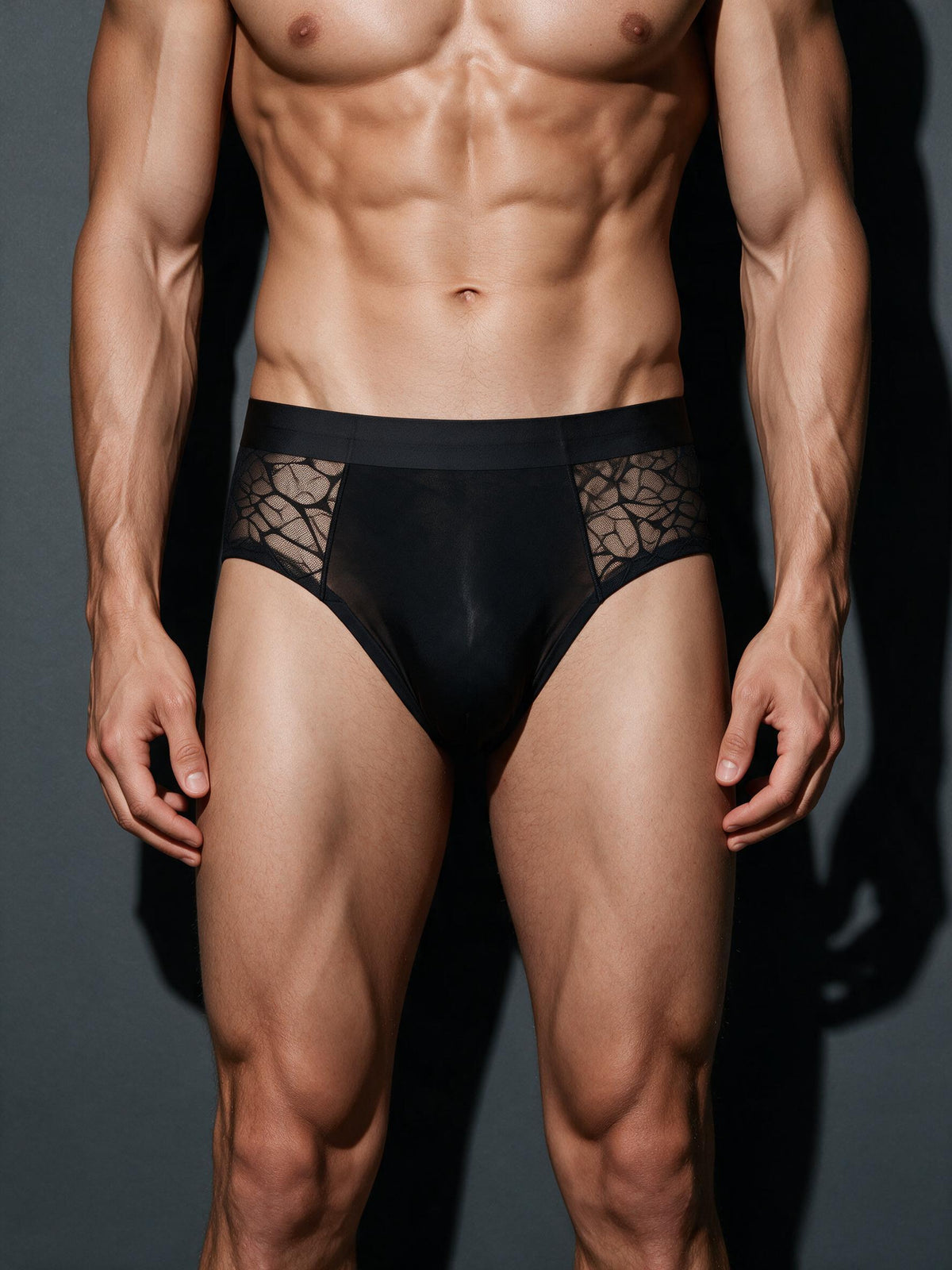 Male model wearing a black sheer geometric lace men's brief, front view showcasing the smooth nude-feel ice silk pouch and breathable lace side panels.