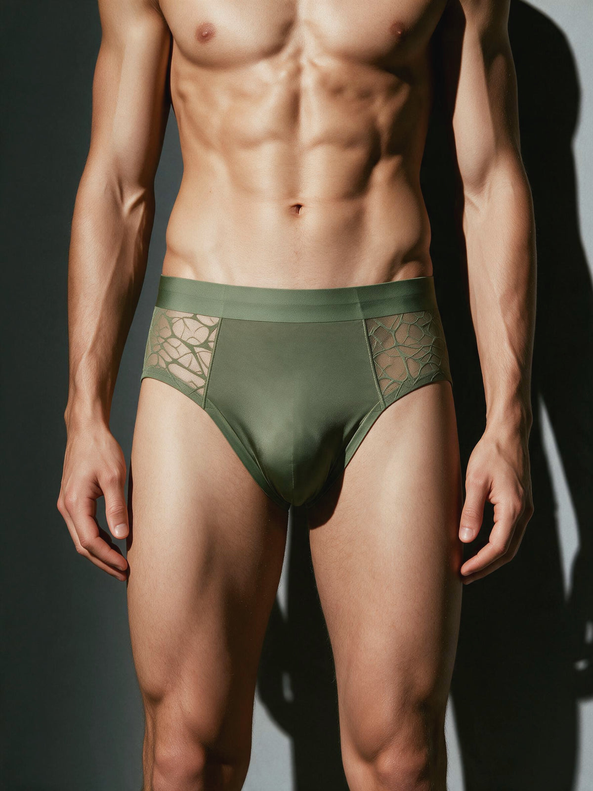 Male model wearing a Matcha Green sheer geometric lace men's brief, front view showcasing the smooth nude-feel ice silk pouch and breathable lace side panels.