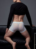 Back view of a male model leaning on a black sofa, wearing the ILLUSION white mesh lace trunks, showing the high-stretch, body-contouring silhouette that prevents rolling.