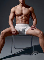 Front view of an athletic male model seated, wearing the Velvet Fluxe ILLUSION white ultra-thin sheer boxer briefs, demonstrating a comfortable bare-sensation fit.