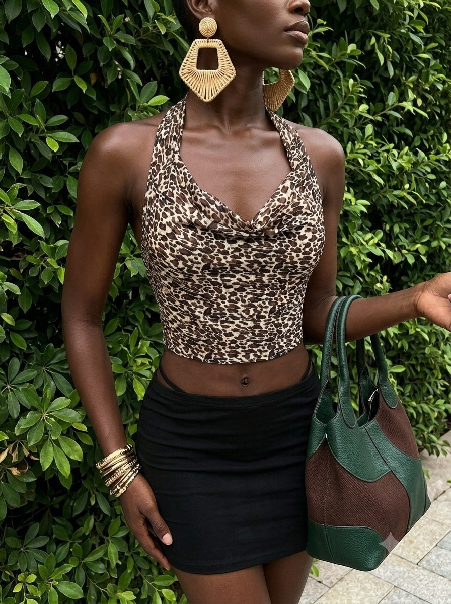 An outdoor fashion shot of a model against green foliage wearing a versatile lingerie-as-outerwear ensemble. She is styled in a leopard-print halter top with ruched detailing designed for braless comfort, paired seamlessly with a black bodycon mini skirt and matching thong. The look is accessorized with statement gold earrings and a handbag, perfectly capturing a trend-forward Y2K summer aesthetic.
