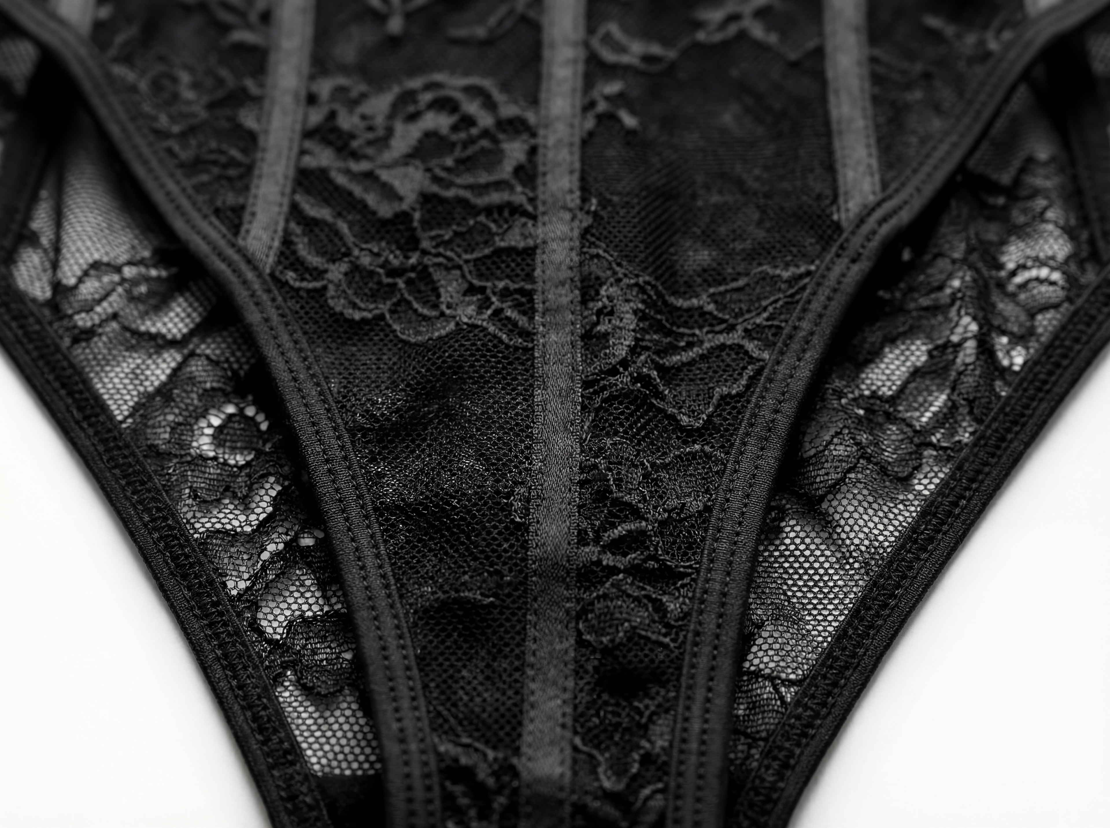Close-up shot of black lace panties featuring sheer mesh fabric, intricate floral embroidery, and sleek black satin strapping. Detail of elegant women's intimates, high-cut lace underwear, and luxury bodysuit construction.