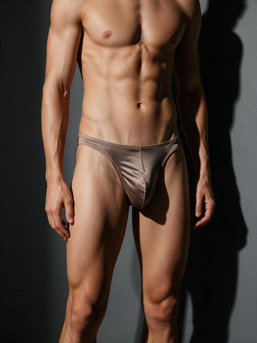 Front view of a male model wearing the Velvet Fluxe brown ice silk satin brief, highlighting the low-rise thin side straps, seamless edging, and 3D enlarged enhancing pouch.