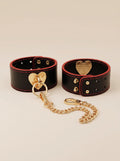 Full set of Velvet Fluxe VALENTINA luxury black leather and gold heart cuffs. Includes a detachable gold chain, adjustable studs, and crimson red accents. The ultimate high-end intimate accessory for romantic gifting and boudoir styling.