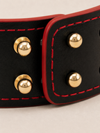 Detail of the adjustable multi-stud closure on the Velvet Fluxe black leather cuff, highlighted by vibrant crimson red contrast stitching. Designed for a custom, secure fit for wrists or ankles.