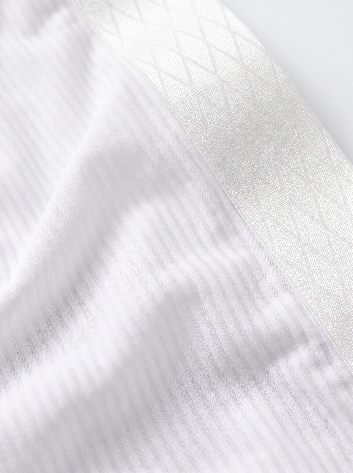 Close-up texture detail of Velvet Fluxe men's white ribbed cotton briefs, featuring breathable multidirectional stretch fabric and a geometric diamond-patterned waistband.