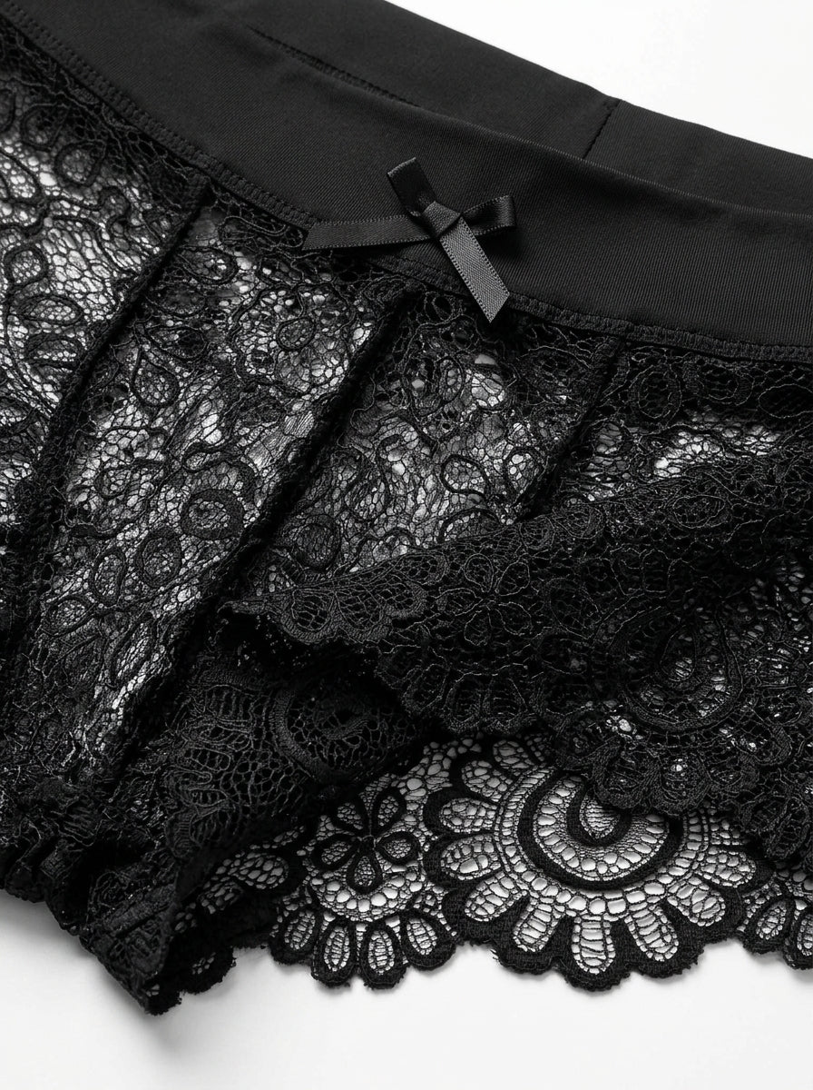 Close up of Velvet Fluxe NOCTURNE French men's sheer black lace boxer briefs. Product view showing the intricate floral lace pattern, solid black elastic waistband for support, and a subtle center bow detail.