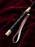 Detail shot of the Velvet Fluxe FELINA cat paw paddle handle. Highlighting the textured black grip, premium gold-tone hardware, and genuine leather wrist loop against a rich red velvet background.