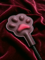 Close-up of the Velvet Fluxe FELINA thermo-reactive paw paddle head. The 3D pads transition to a vibrant red, demonstrating the heat-sensitive color-changing effect on a dark red velvet drape.